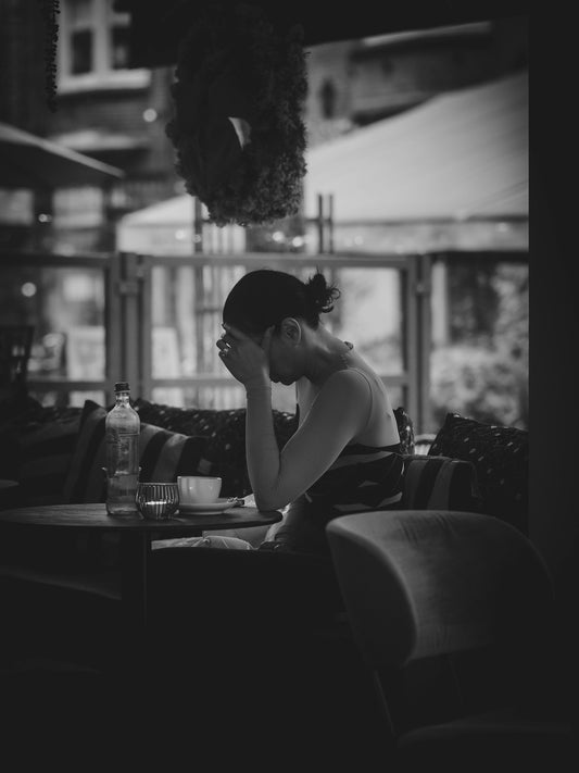 A woman sitting at a cafe table with her head in her hands